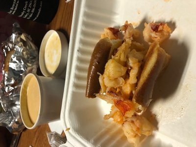 Half of a lobster roll dripped with butter, lobster bisque